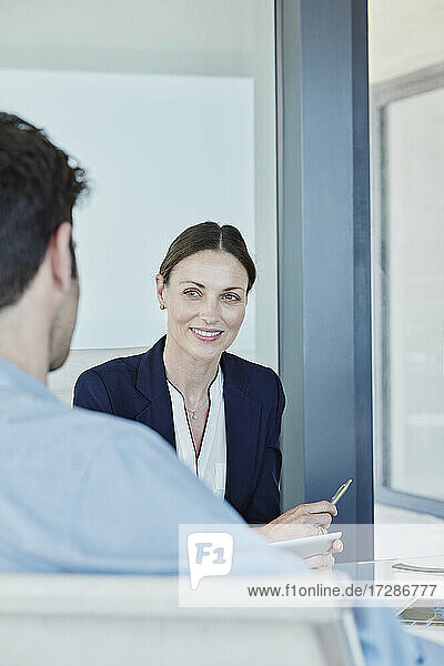 Lächelnde Immobilienmaklerin  die einen männlichen Kunden ansieht  während sie ein Gespräch führt