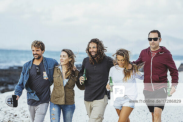 Männer und Frauen mit Bierflaschen gehen zusammen am Strand spazieren