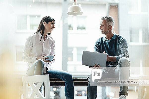 Männlicher Unternehmer  der einen Laptop hält  während er mit einer Kollegin in einem Café diskutiert