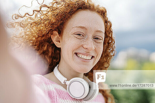 Fröhliche junge Frau mit lockigem Haar und Kopfhörern