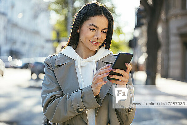 Smiling woman using smart phone in city