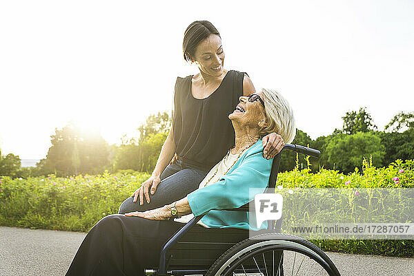 Enkelin lächelt  während sie die im Rollstuhl sitzende Großmutter betrachtet