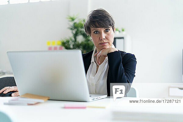 Businesswoman sitting with hand on chin at desk in office