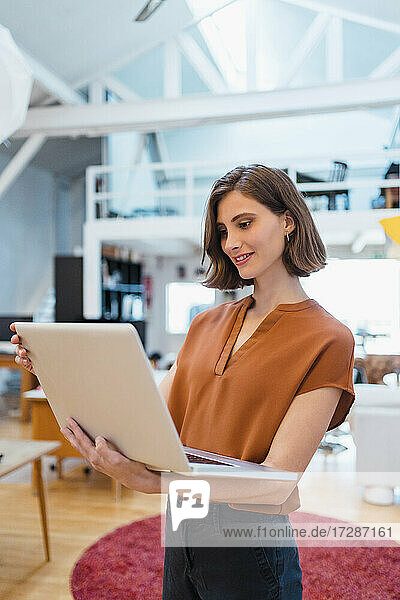 Schöne junge Geschäftsfrau mit braunen Haaren  die einen Laptop benutzt  während sie im kreativen Büro arbeitet