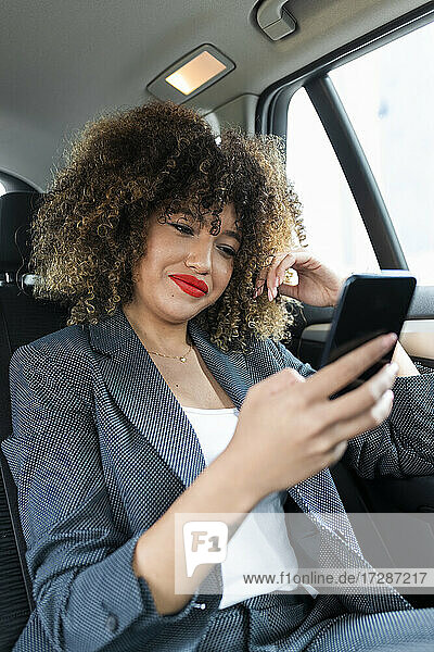 Weibliche Fachkraft mit lockigem Haar  die im Auto sitzend ein Mobiltelefon benutzt