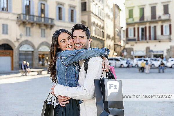 Smiling tourist couple holding shopping bags while embracing at city