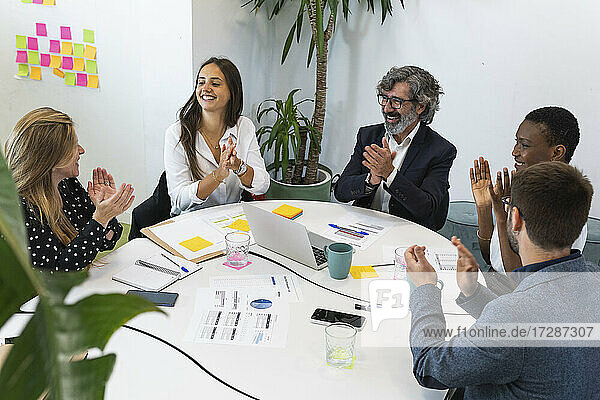Aufgeregte Unternehmer und Unternehmerinnen klatschen am Tisch im Büro