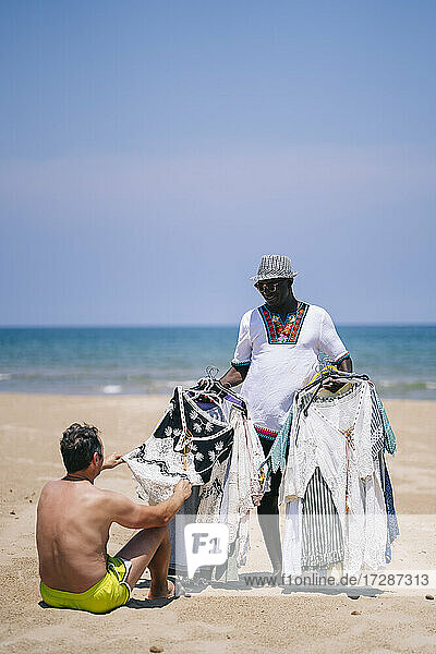 Man buying clothes from male vendor at beach during sunny day