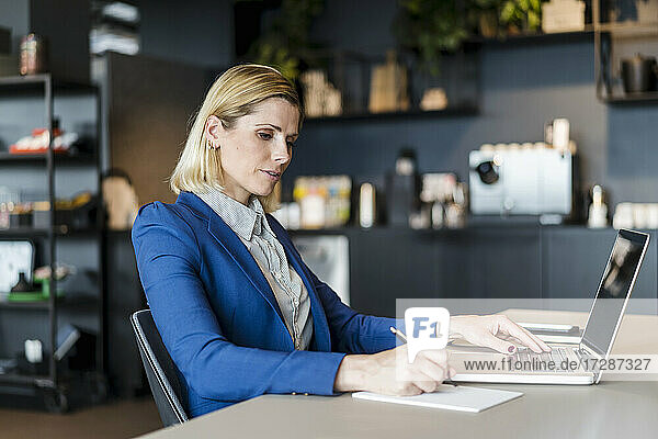 Blonde Geschäftsfrau  die mit einem Laptop am Schreibtisch im Büro sitzt und schreibt