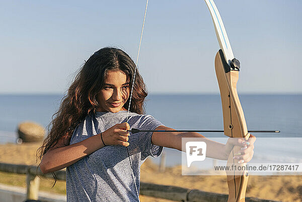 Smiling young woman practicing archery during sunny day