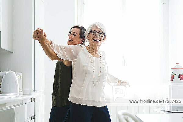 Glückliche ältere Frau tanzt mit Enkelin in der Küche zu Hause