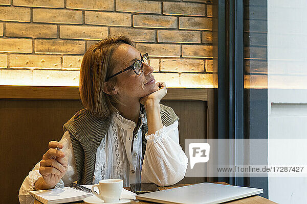 Frau mit Hand am Kinn träumt  während sie durch das Fenster eines Cafés schaut