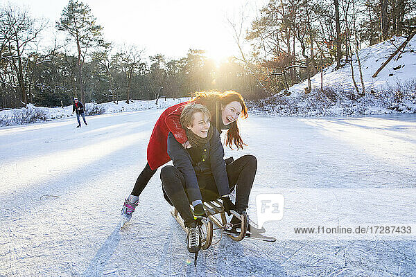 Fröhliches Paar beim Schlittenfahren und Schlittschuhlaufen auf einem zugefrorenen See