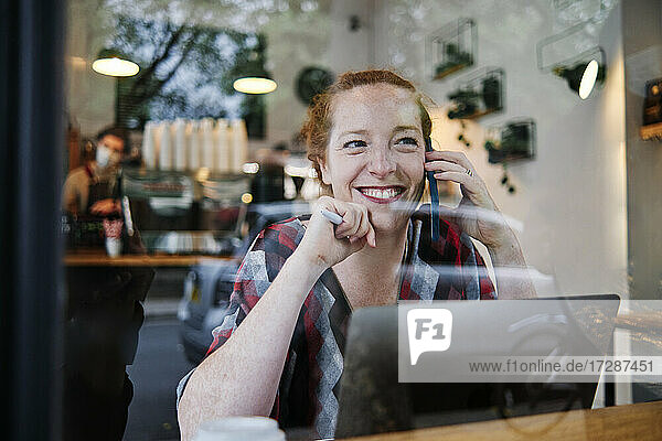 Lächelnde Frau  die wegschaut  während sie in einem Café mit ihrem Smartphone telefoniert