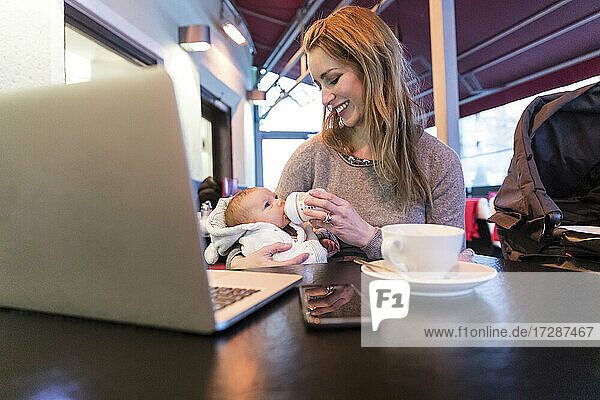 Lächelnde Mutter füttert ihr kleines Mädchen mit Milch  während sie sich von einem Café aus selbstständig macht