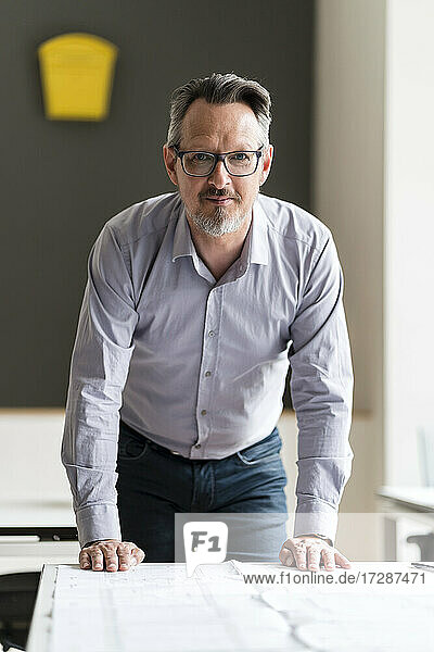 Businessman with blueprint leaning on desk at office