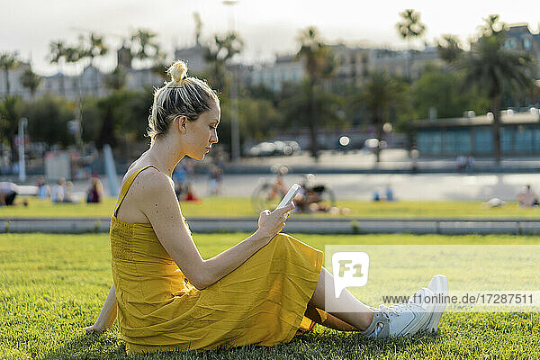 Frau  die im Gras sitzend eine SMS über ihr Mobiltelefon verschickt