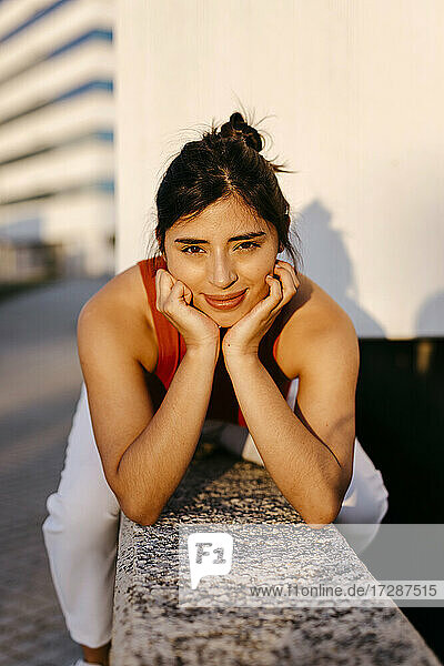 Young woman with hand on chin sitting on retaining wall