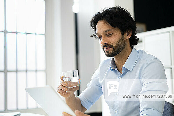 Businessman with drinking glass using digital tablet in office