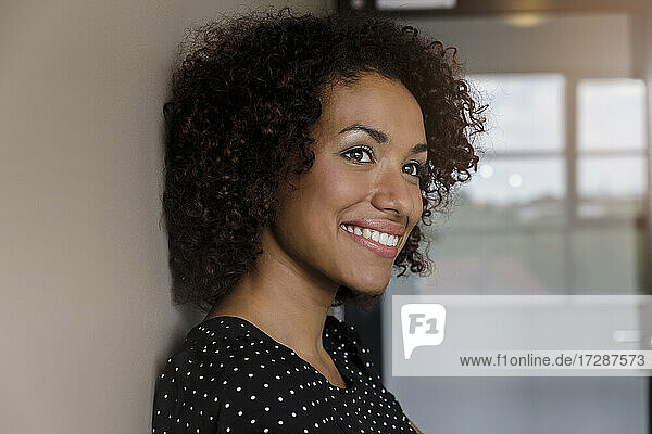 Smiling young businesswoman with curly hair in office looking away