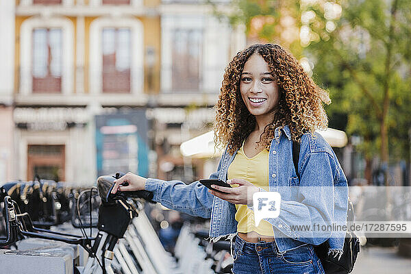 Lächelnde Frau mit Smartphone in der Nähe einer Fahrradabstellanlage