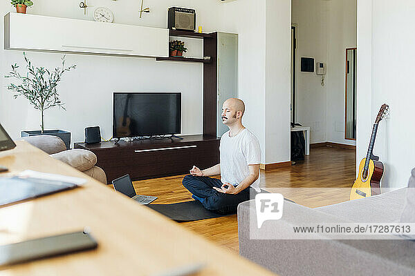 Junger Mann  der zu Hause über seinen Laptop online Yoga lernt