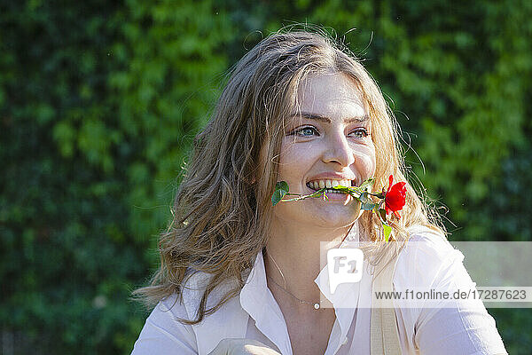 Junge Frau mit Freesienblüte im Mund schaut weg
