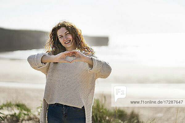 Lächelnde junge Frau mit Herzform am Strand