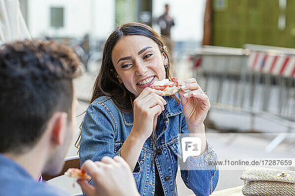 Junge Frau mit Pizzastück lächelt und sieht einen Mann an