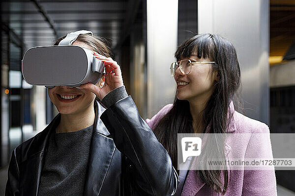 Unternehmerin mit Virtual-Reality-Headset und lächelndem Kollegen im Hintergrund