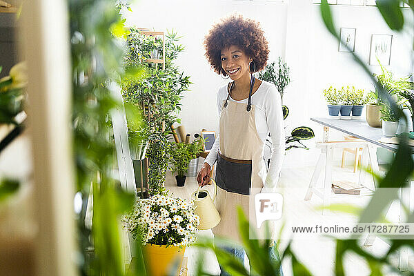 Female florist smiling while watering plant at shop
