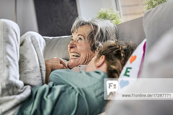 Fröhliche Großmutter liegt neben ihrer Enkelin auf dem Sofa zu Hause
