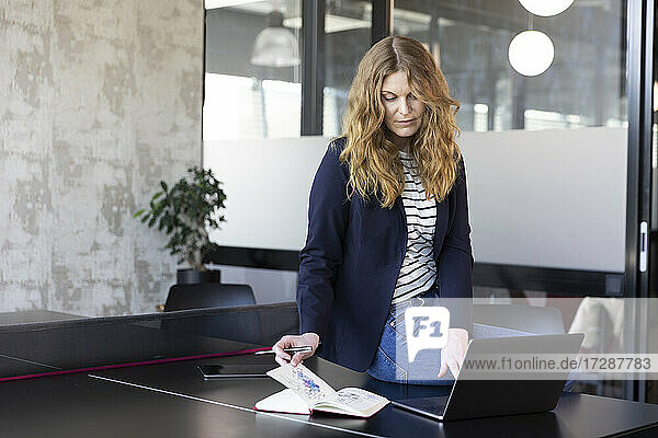 Female entrepreneur with diary using laptop on table at office