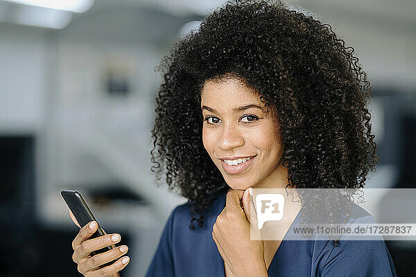 Schöne Geschäftsfrau mit Mobiltelefon im Büro stehend