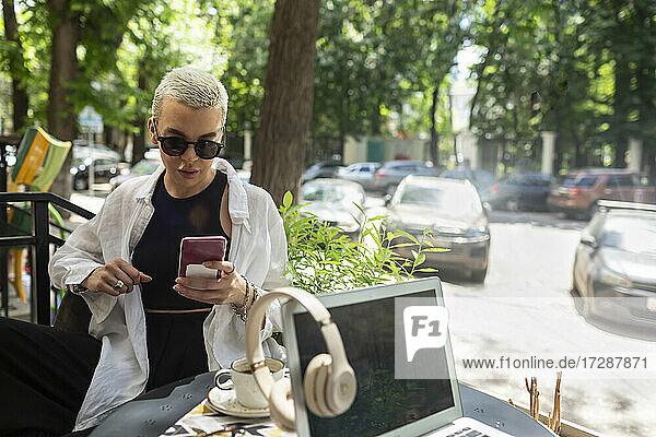 Mittlere erwachsene Frau mit Sonnenbrille  die ein Smartphone benutzt  während sie in einem Café sitzt