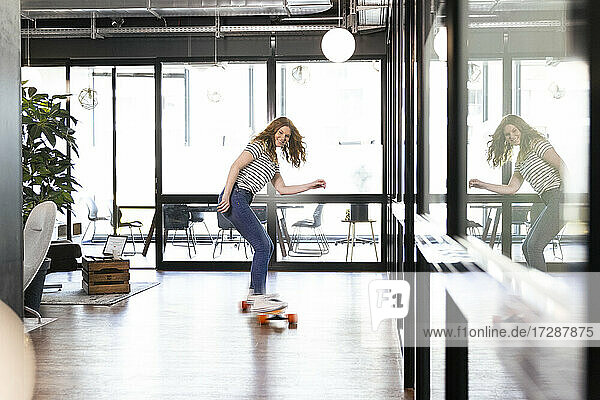 Smiling creative businesswoman skateboarding in office