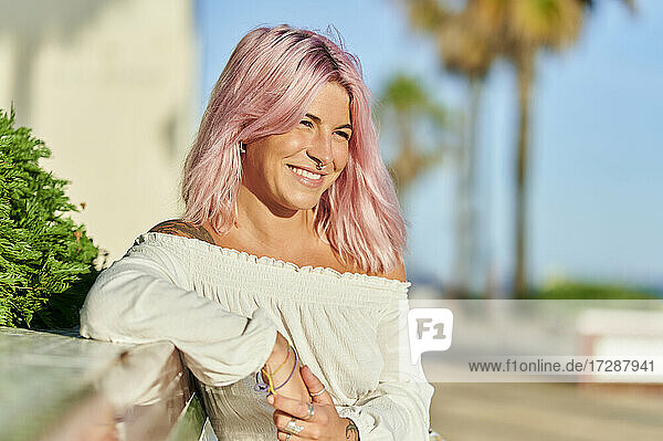 Lächelnde Hipster-Frau  die sich an einer Stützmauer an einem sonnigen Tag abstützt