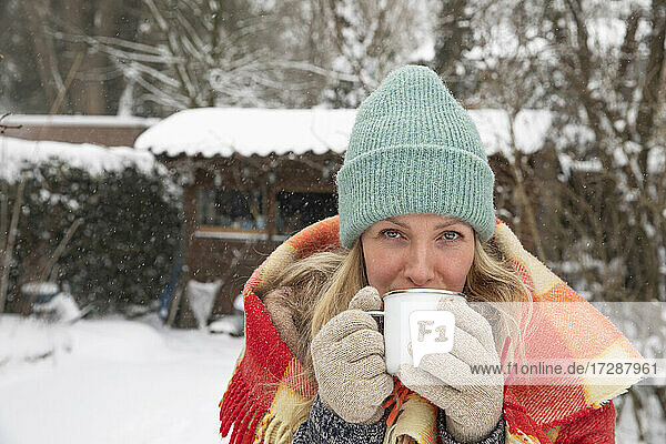 Ältere Frau mit Strickmütze trinkt Kaffee im Hinterhof bei Schnee