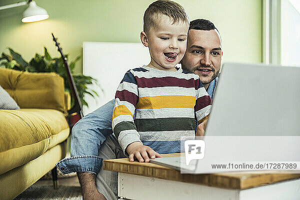 Mann mit Sohn schaut Video auf Laptop im Wohnzimmer zu Hause