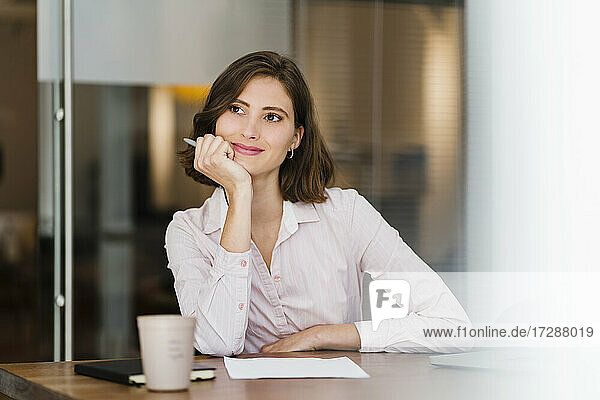 Thoughtful young female professional sitting with hand on chin while looking away