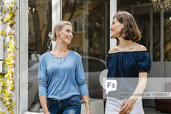 Smiling businesswomen looking at each other while walking outside office