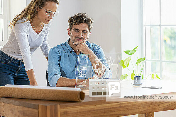 Male and female professional contemplating over transparent digital tablet in office