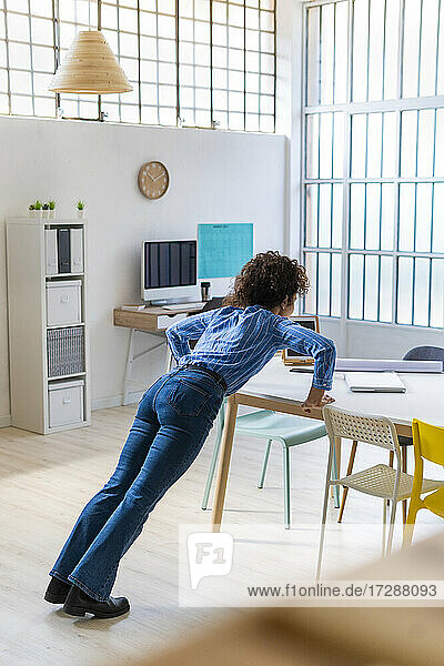 Woman exercising while leaning on desk in office