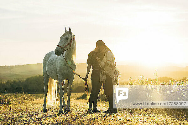 Verliebtes Paar mit Pferd auf einem Feld bei Sonnenuntergang