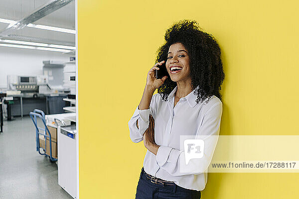 Happy female professional talking on smart phone in front of yellow wall
