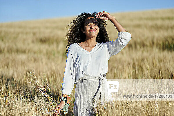 Smiling woman with eyes closed standing in agricultural field during sunny day