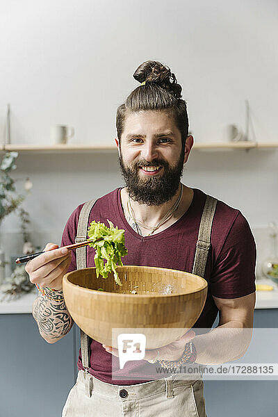 Bearded man smiling while holding salad bowl at home