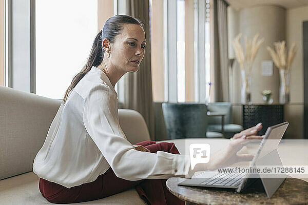 Weibliche Fachkraft  die ein digitales Tablet benutzt  während sie auf dem Sofa im Büro sitzt