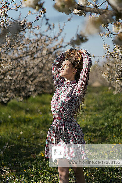 Frau mit Hand im Haar in einem Obstgarten im Frühling stehend