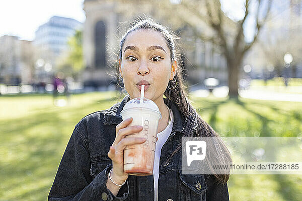Young woman looking cross eyed while drinking milkshake at park
